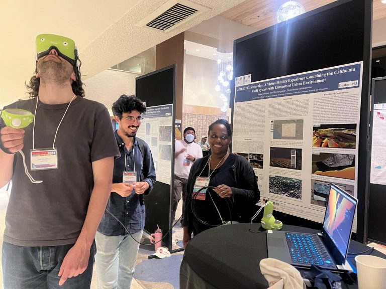 SCEC2024 attendees gathered around a poster, one of which is wearing VR goggles and looking up.